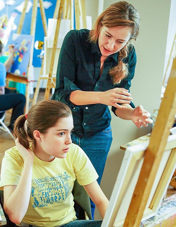 an art teacher mentors a student working on a painting